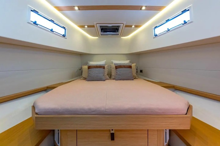 Modern yacht cabin with double bed, cushions, and ambient lighting.