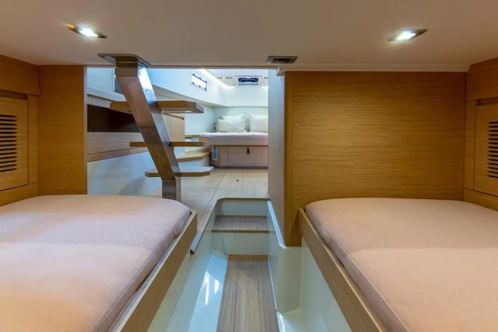 Interior of a boat cabin with two beds, wooden walls, and steps leading to an upper area.