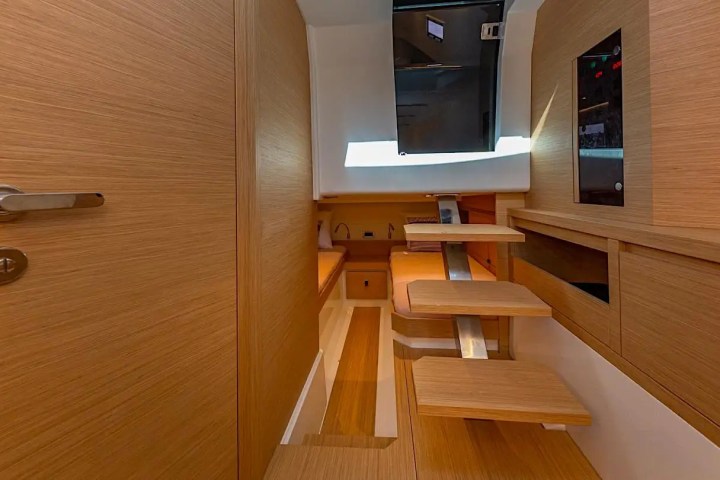 Modern wooden interior with steps leading up to a hatch, featuring sleek cabinetry and door.