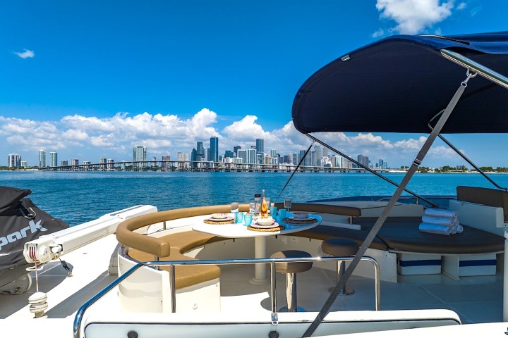 Boat deck with dining area overlooking a city skyline and blue ocean under a bright blue sky.