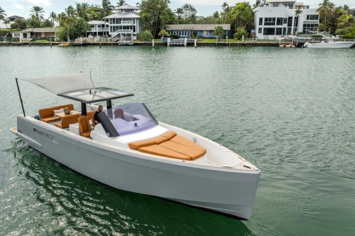 Luxury boat with tan seats on water, houses and trees in background.