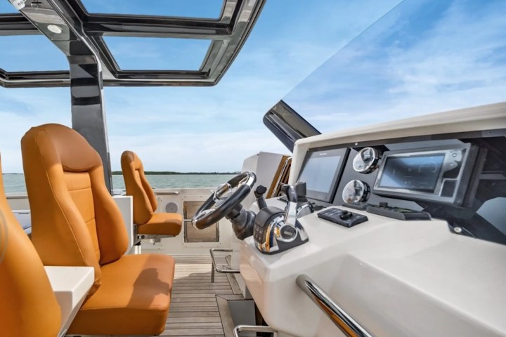 Boat cockpit with orange seats, steering wheel, and control panel against a blue sky.