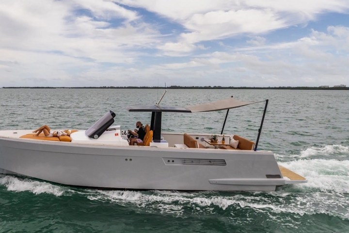 Modern boat with sunbathing area on a calm sea, blue sky with clouds overhead.