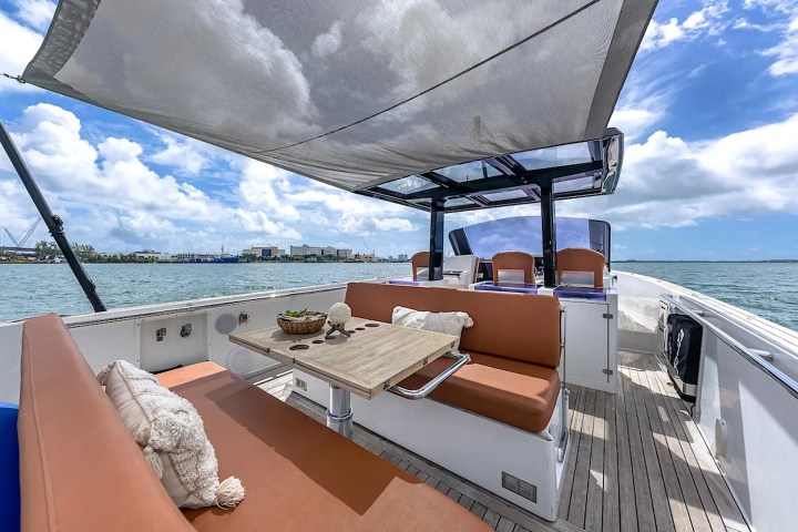 Luxury yacht deck with seating, a table, and a sunshade, set against a sunny ocean and blue sky backdrop.