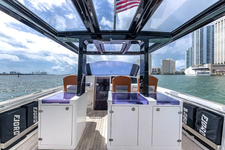 Interior of a modern boat with seats and an American flag, city skyline in background.