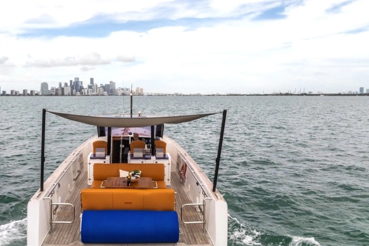 Boat with seating area on water, city skyline in background, under a partly cloudy sky.