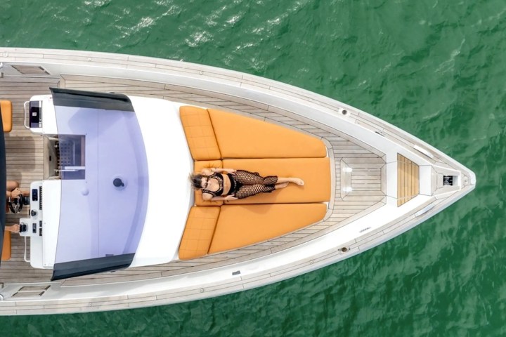 Aerial view of a person sunbathing on a yacht with orange cushions in green water.
