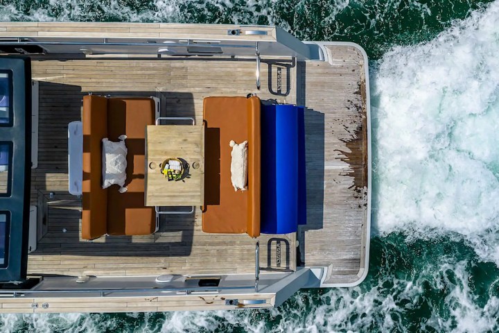 Top view of a yacht deck with seating area and table, wake trailing in the ocean.
