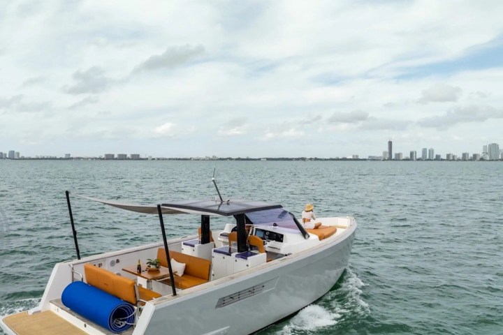 A boat with orange seating and canopy on a body of water with a city skyline in the distance.