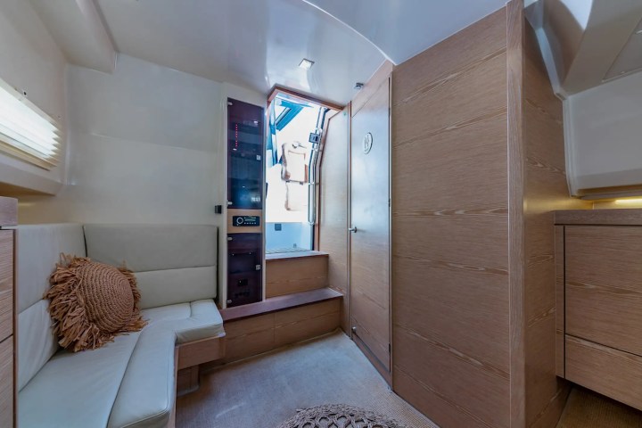 Boat cabin with beige sofa, round cushion, and wooden panel walls, leading to a stairway and exit door.