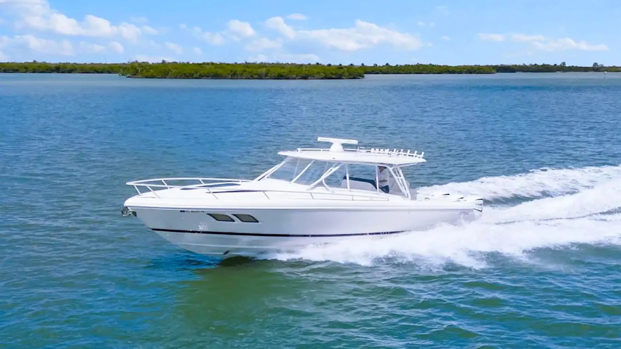 White motorboat speeding on blue water with green shoreline in background.