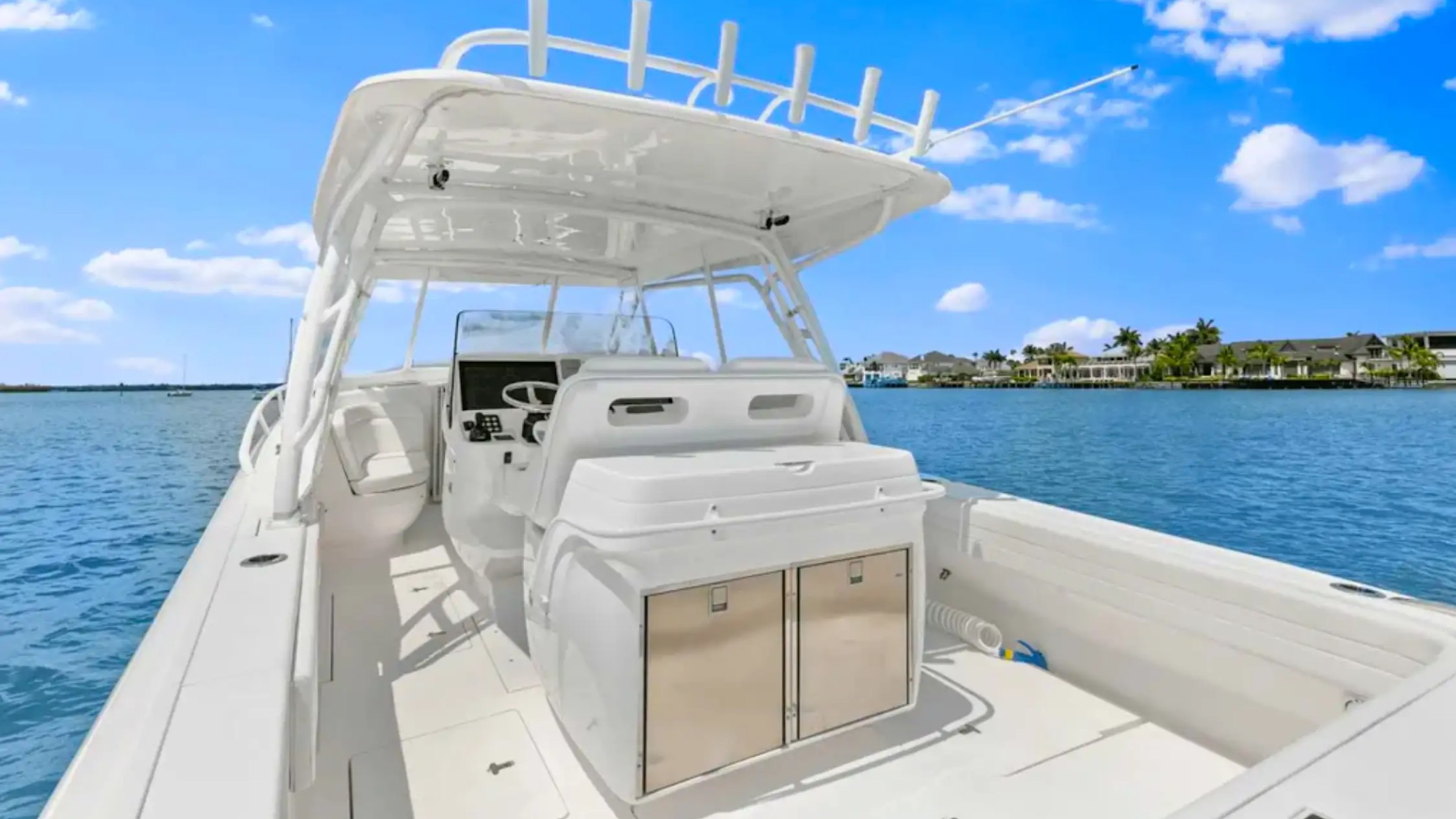 White boat interior with helm, chairs, and cabinets on a sunny day by the water.
