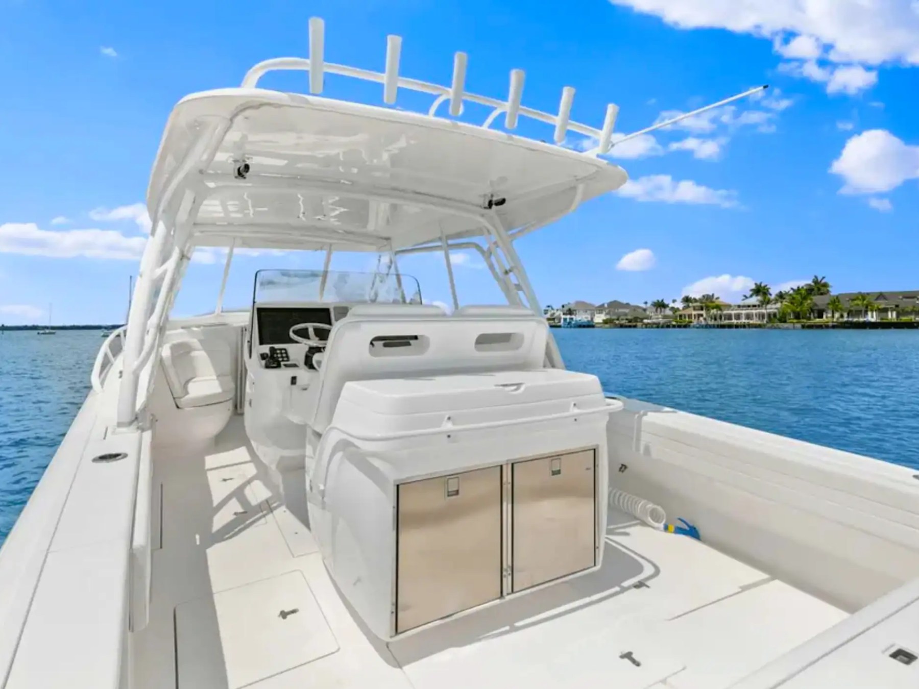 White boat interior with helm, chairs, and cabinets on a sunny day by the water.