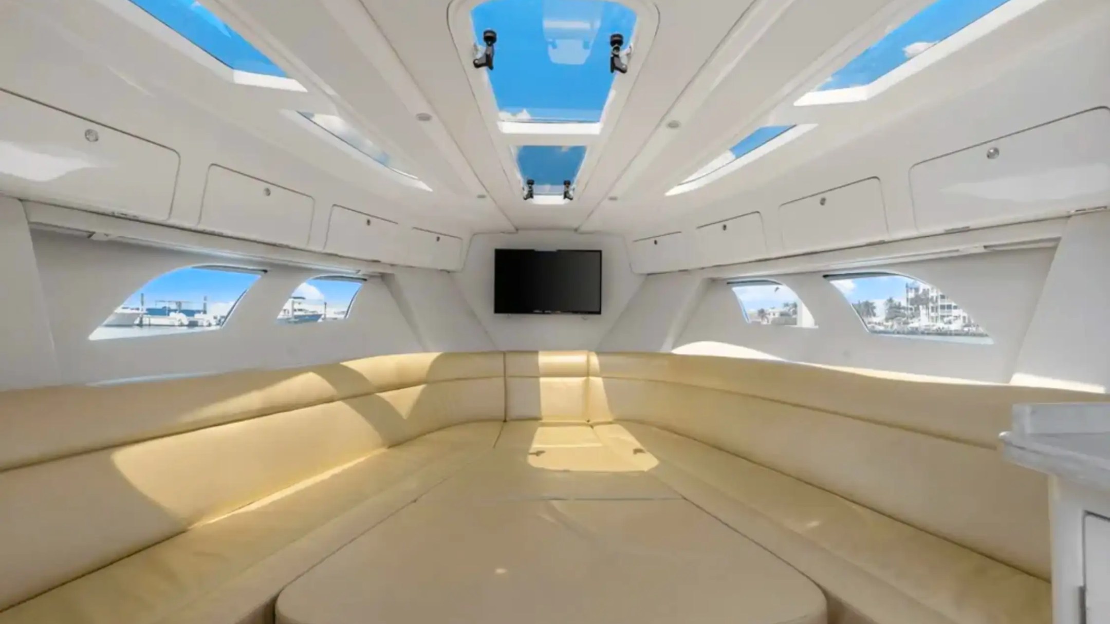 Interior view of a yacht cabin with beige seating, skylights, and a wall-mounted TV.