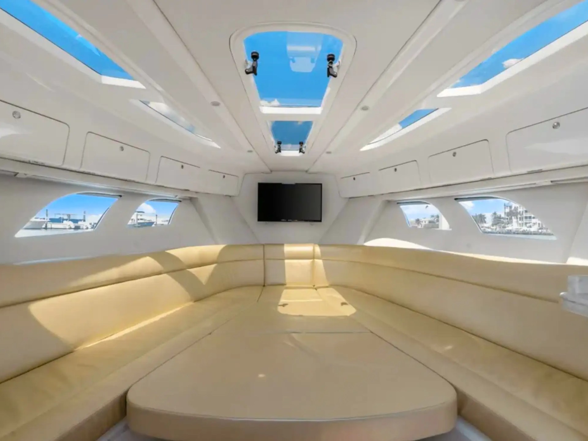 Interior view of a yacht cabin with beige seating, skylights, and a wall-mounted TV.