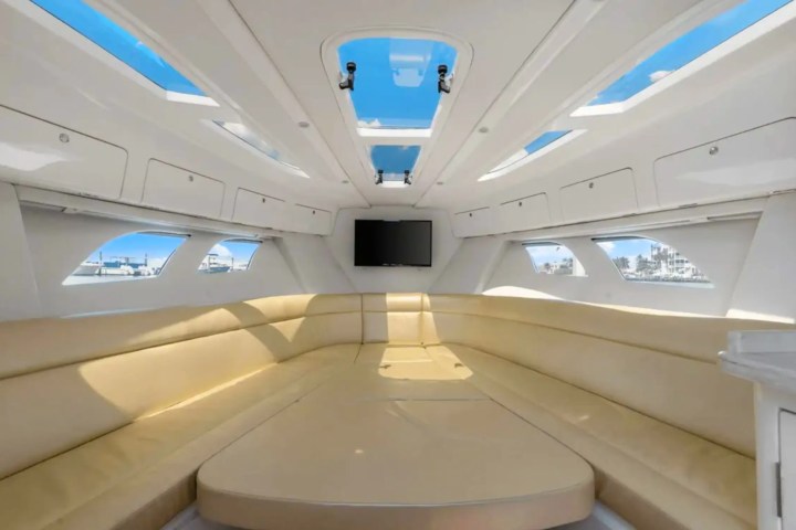 Interior view of a yacht cabin with beige seating, skylights, and a wall-mounted TV.