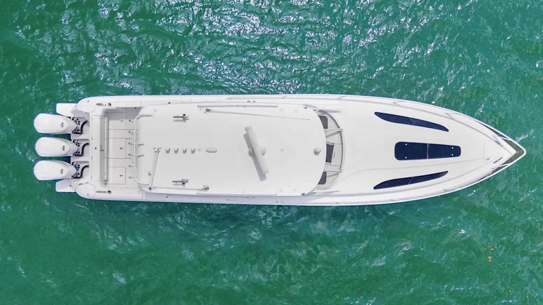 Aerial view of a white speedboat with three engines on green water.