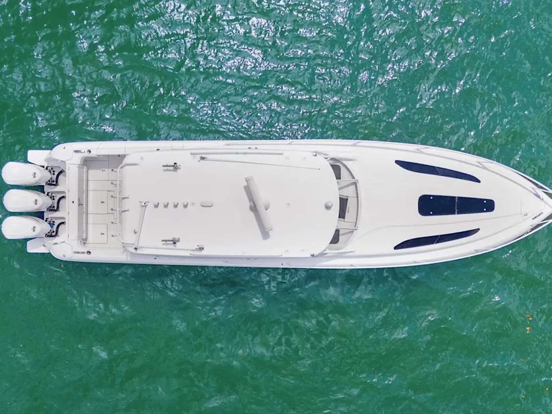 Aerial view of a white speedboat with three engines on green water.