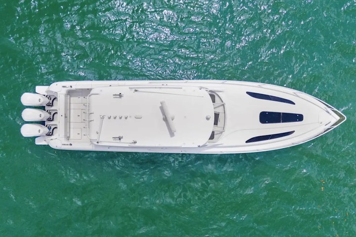 Aerial view of a white speedboat with three engines on green water.