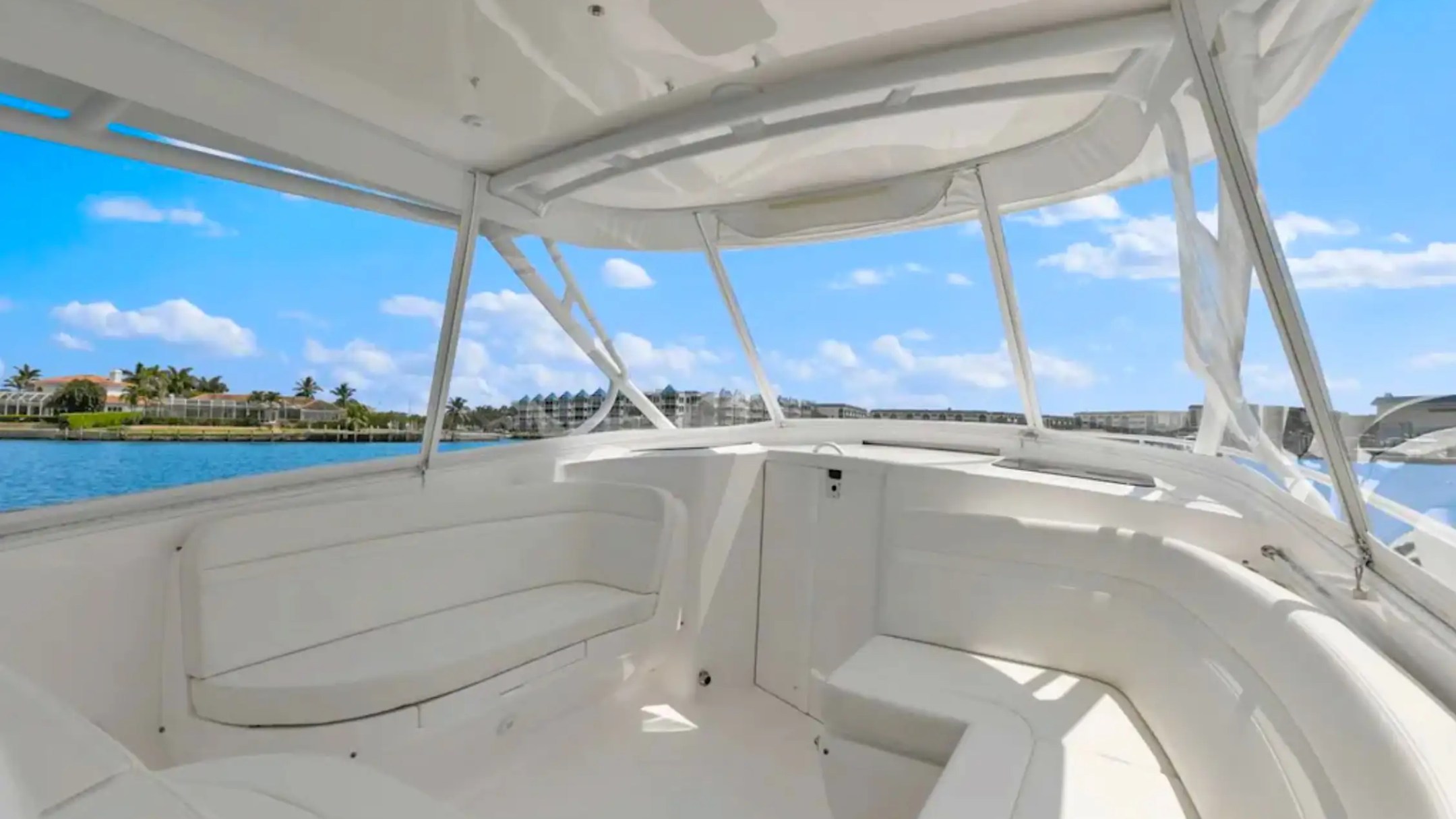 Interior of a white boat with seating, overlooking water and palm trees under a blue sky.