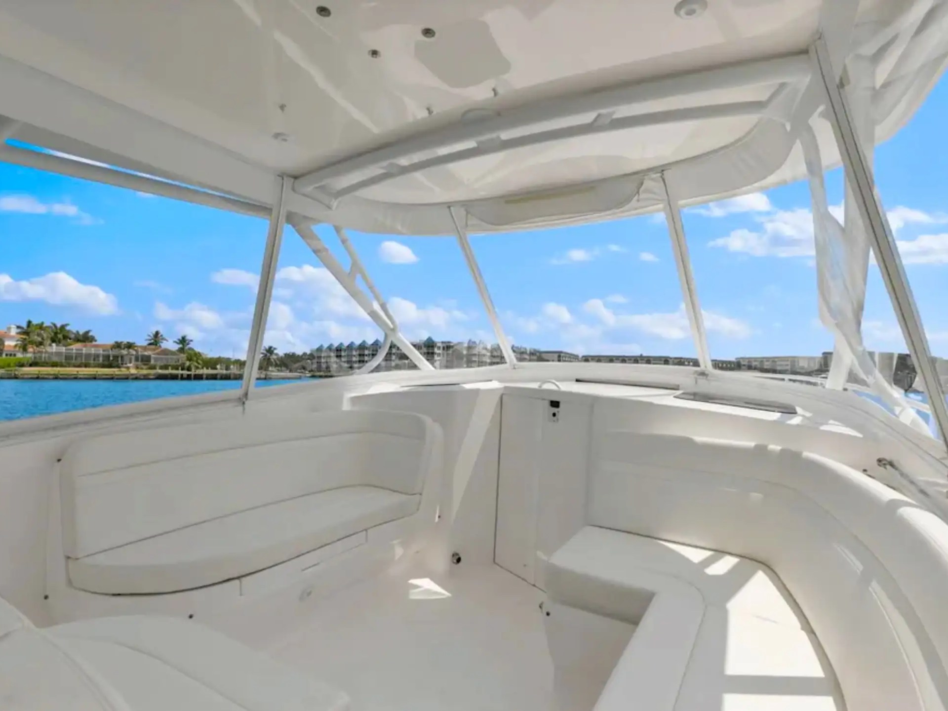 Interior of a white boat with seating, overlooking water and palm trees under a blue sky.