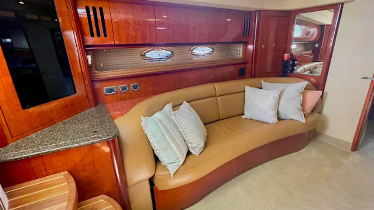 Luxurious yacht interior with curved tan sofa, decorative pillows, wooden cabinets, and oval windows.
