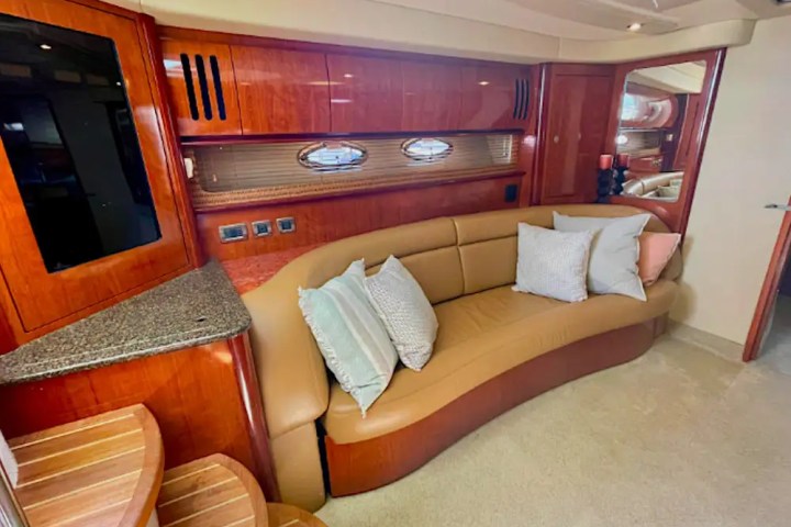Luxurious yacht interior with curved tan sofa, decorative pillows, wooden cabinets, and oval windows.