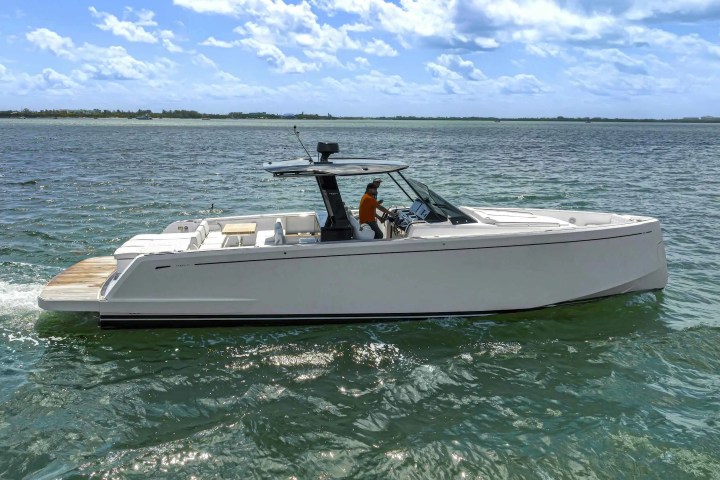 White yacht on open water with a person at the helm under a cloudy sky.