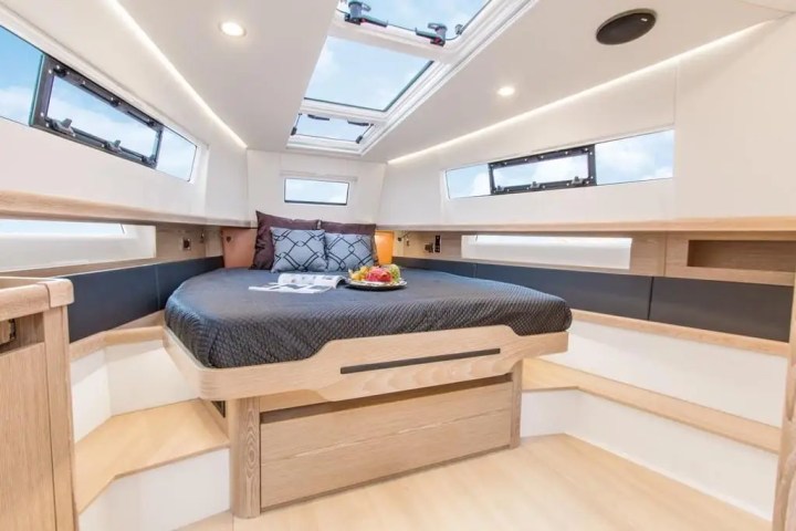 Boat cabin with a central bed, skylights, and wooden interior accents.