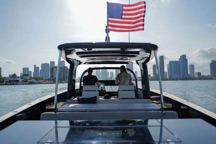 View from back of boat with two people, US flag, city skyline in the background.
