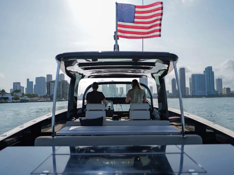 View from back of boat with two people, US flag, city skyline in the background.