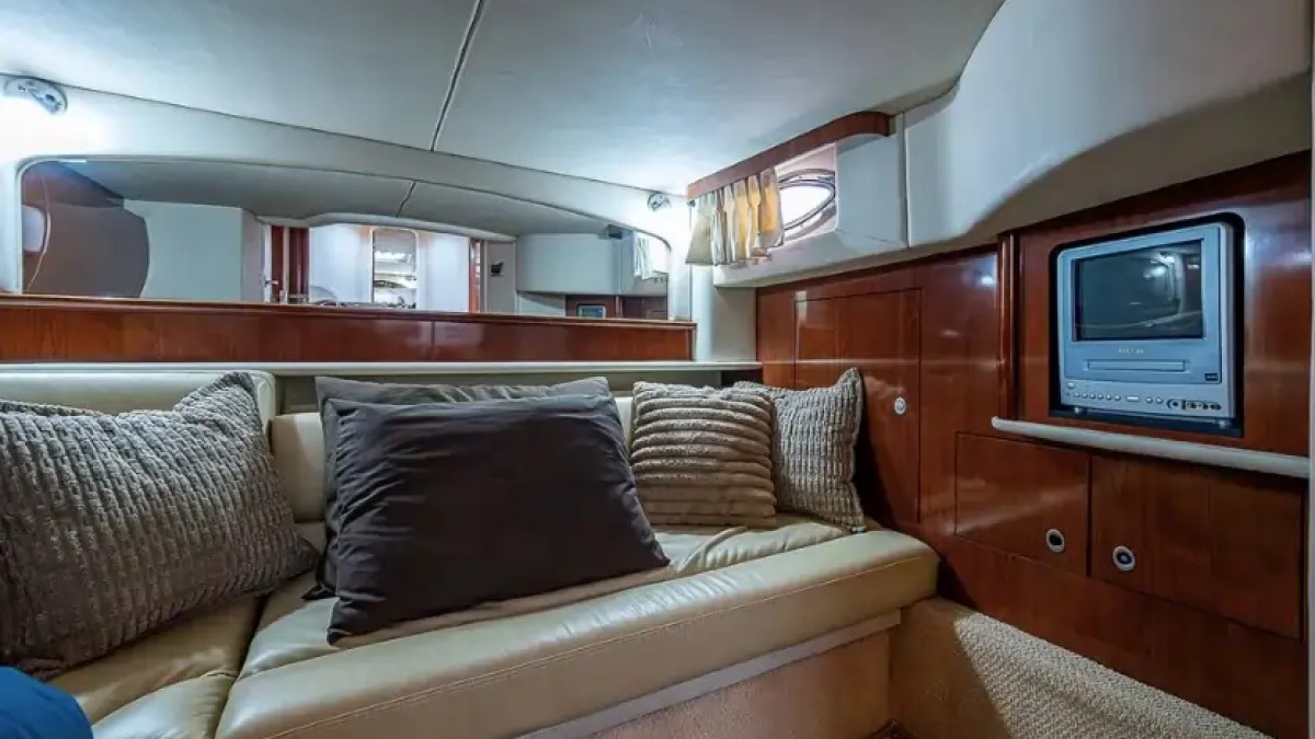Cozy yacht cabin with beige couch, pillows, wood paneling, and small TV.