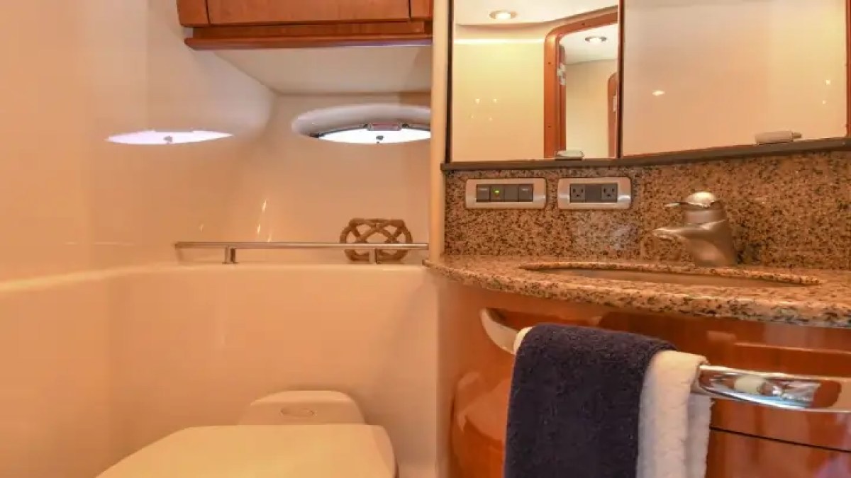 Compact boat bathroom with sink, toilet, towel rack, and porthole window.