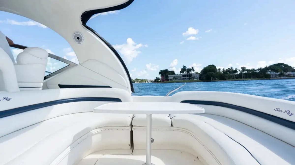 White yacht interior with table, view of sea and distant shore with trees.
