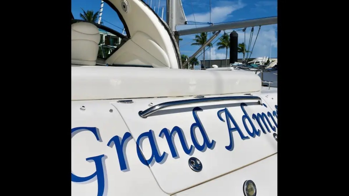 Side of a white boat named 'Grand Admiral' with palm trees in background.