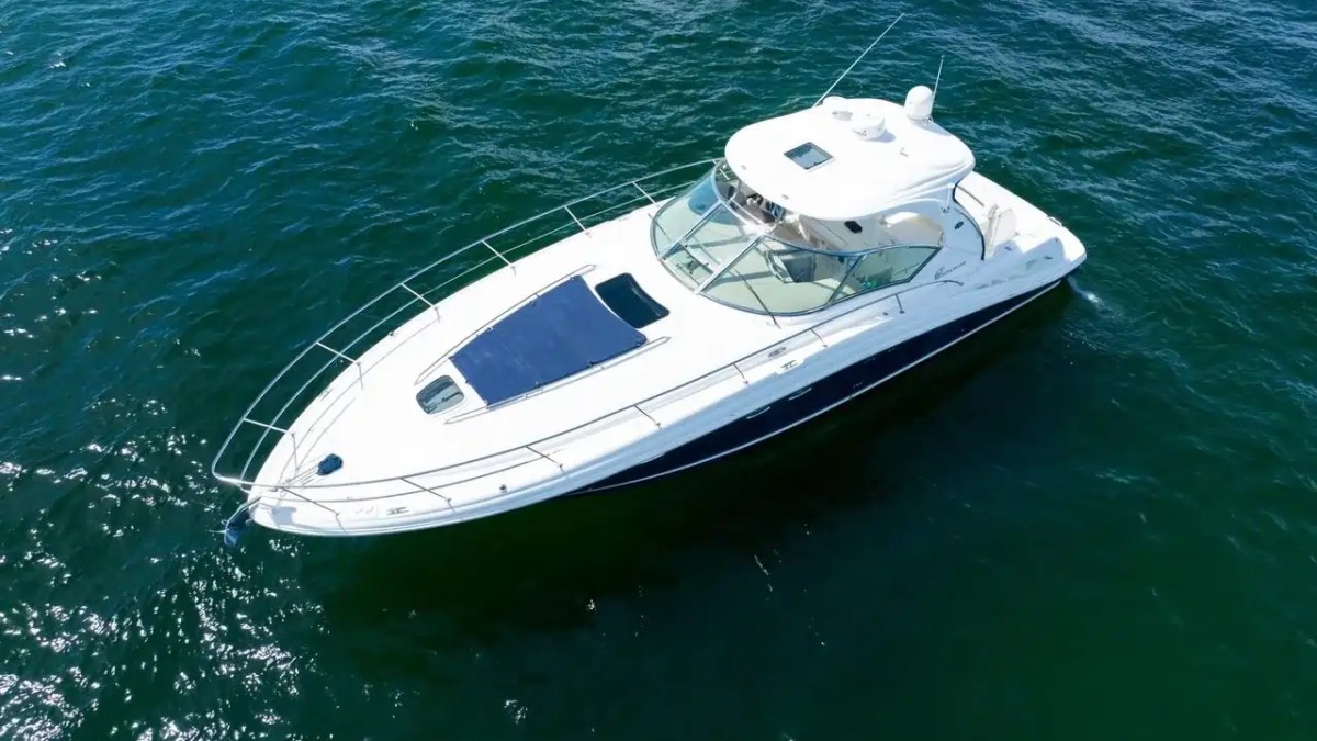 Aerial view of a white motor yacht on calm blue water.