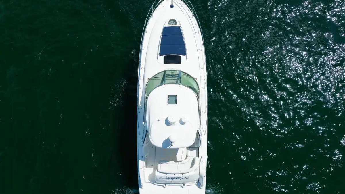 Aerial view of a white yacht sailing on dark green water.