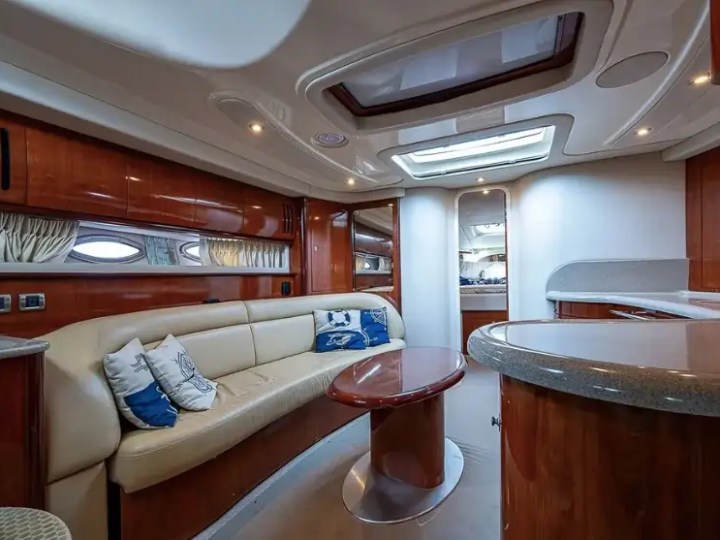 Luxurious yacht interior with beige sofa, oval table, wood paneling, and skylight.