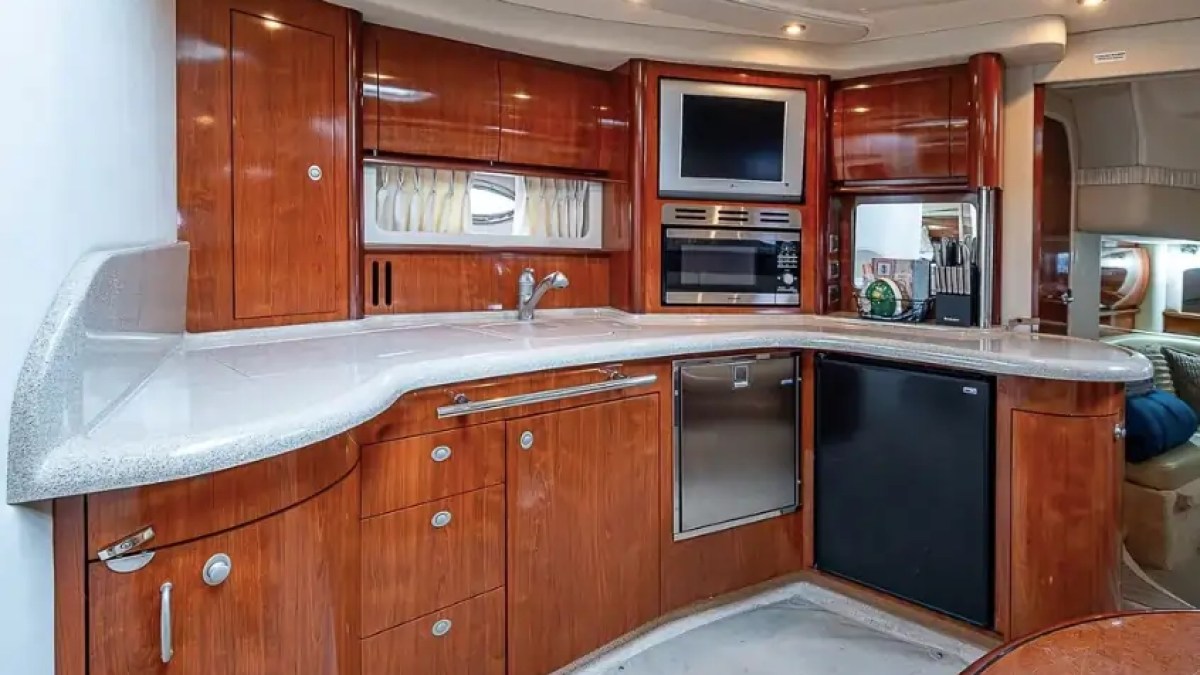 Wood-paneled yacht kitchen with appliances, white countertop, and small fridge.