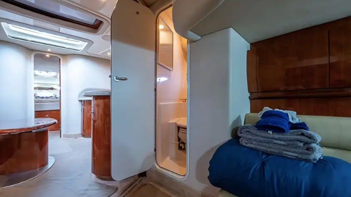Interior of a boat cabin with open door to bathroom and folded towels on a bench.