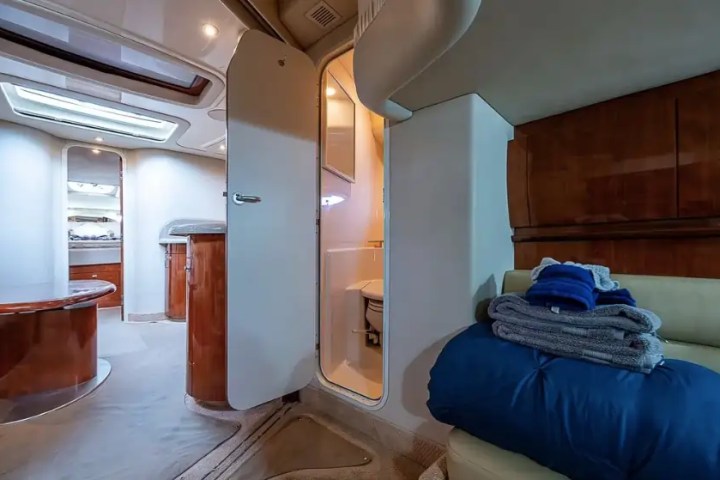 Interior of a boat cabin with open door to bathroom and folded towels on a bench.