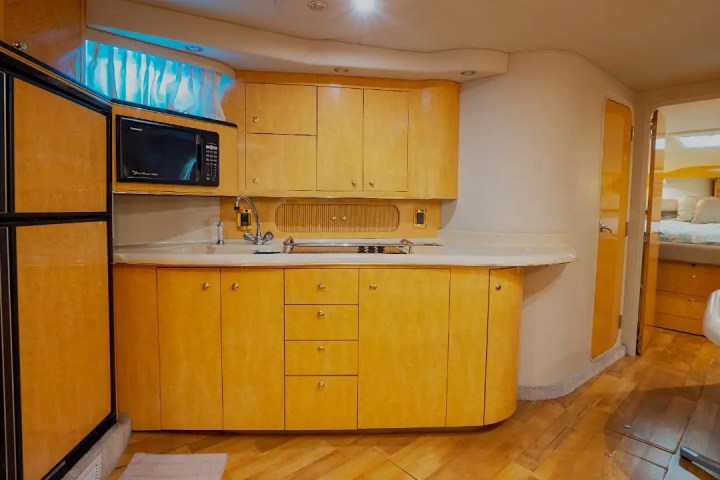 Cozy boat kitchen with wood cabinets, microwave, and small fridge. Doorway leads to sleeping area.