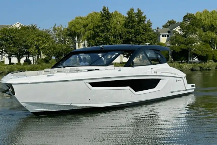 White motorboat on calm water with trees and houses in background.