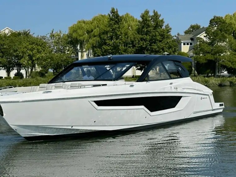 White motorboat on calm water with trees and houses in background.