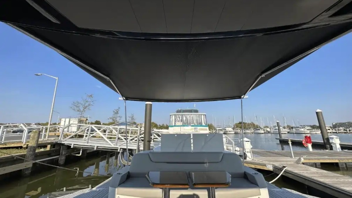 Covered boat deck with seating area in a marina, surrounded by boats and clear sky.