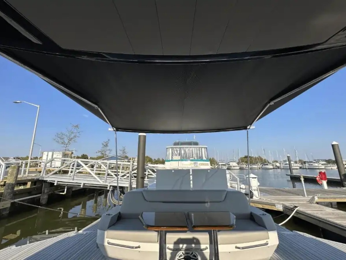 Covered boat deck with seating area in a marina, surrounded by boats and clear sky.