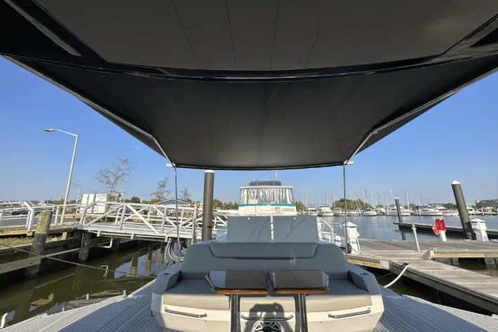 Covered boat deck with seating area in a marina, surrounded by boats and clear sky.