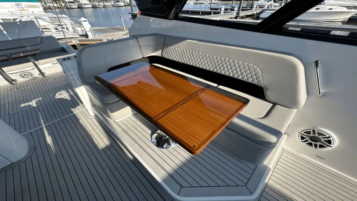 Boat deck with wooden table and cushioned bench seating near a marina.