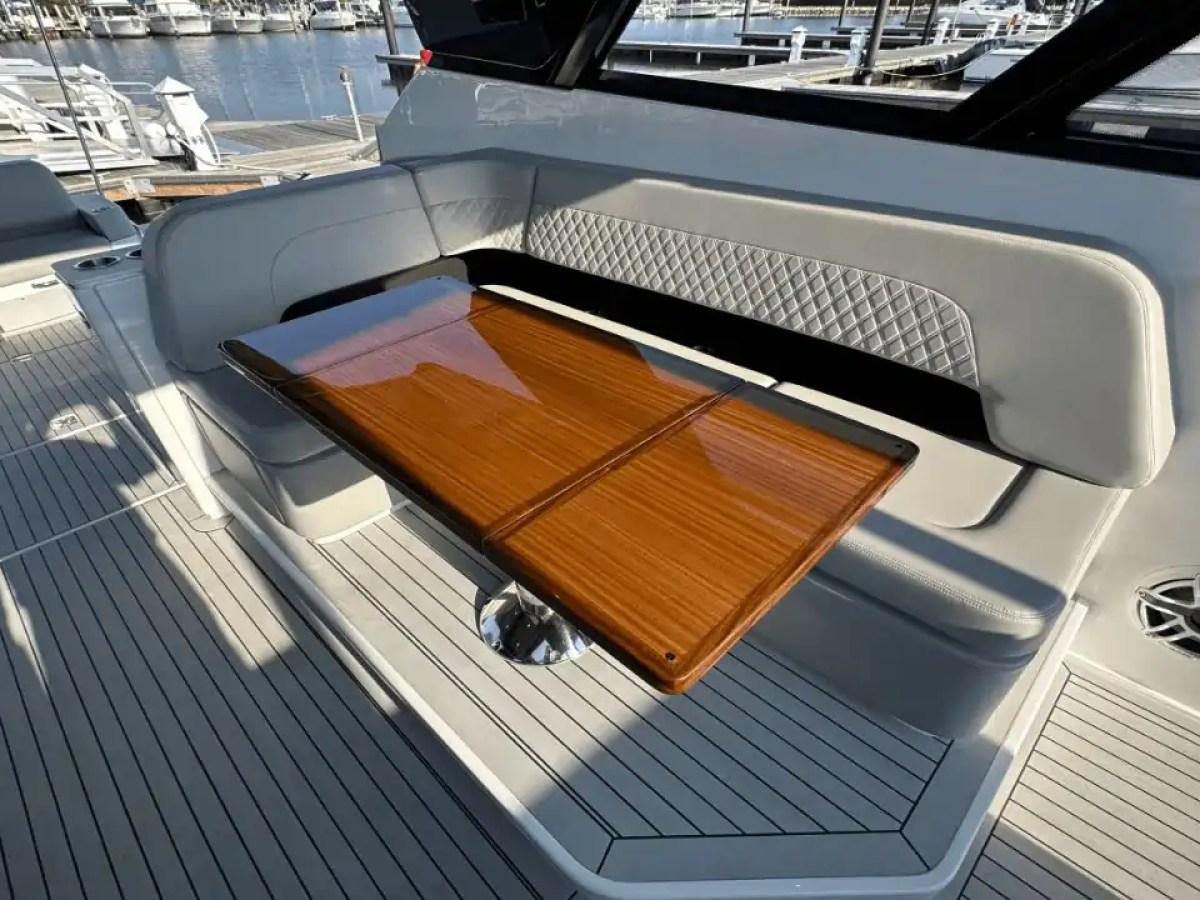 Boat deck with wooden table and cushioned bench seating near a marina.