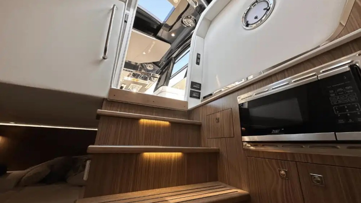 Wooden stairs in a yacht interior with overhead skylight and built-in microwave.